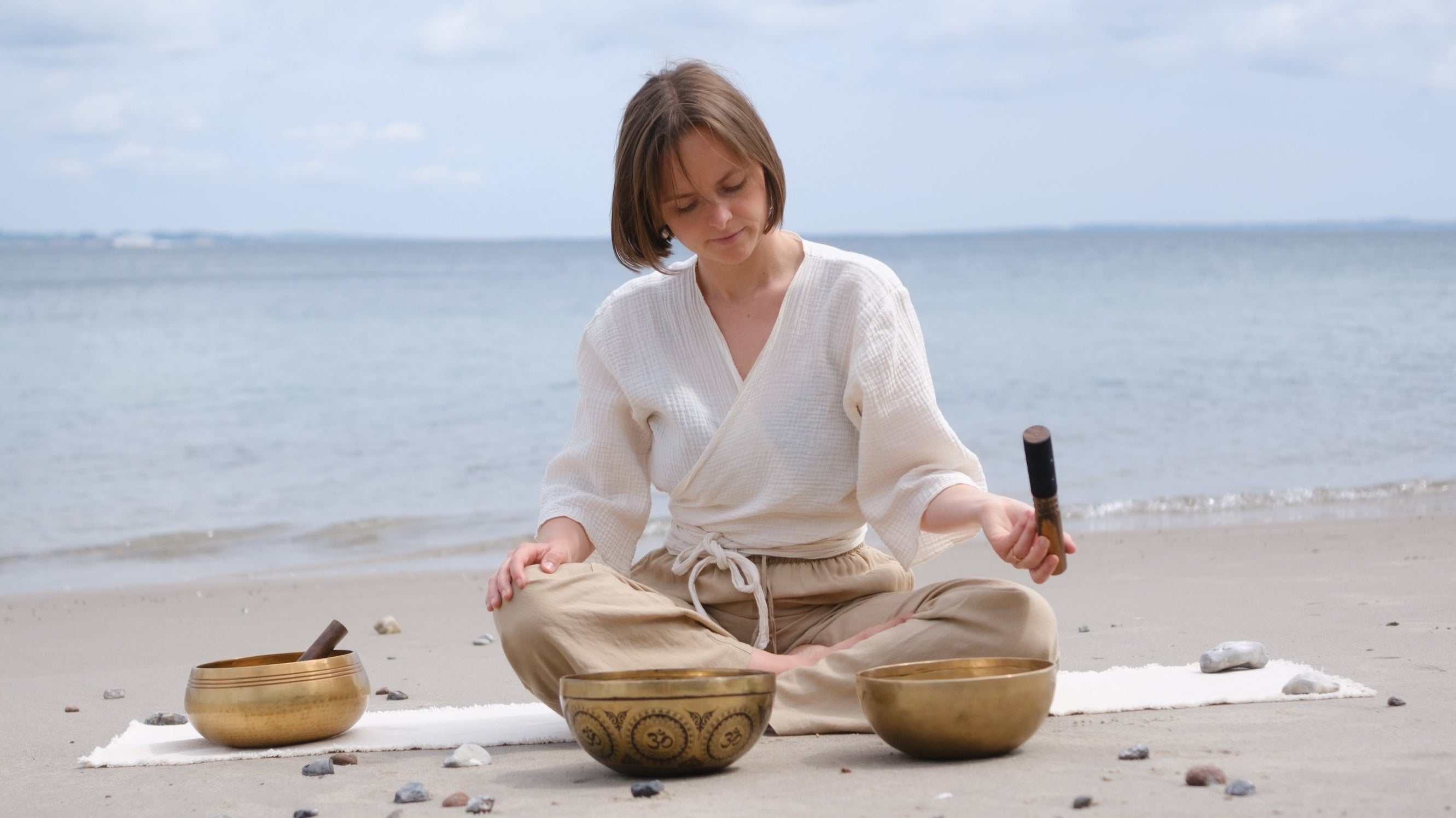 A woman playing couple of singing bowls sitting on a beach