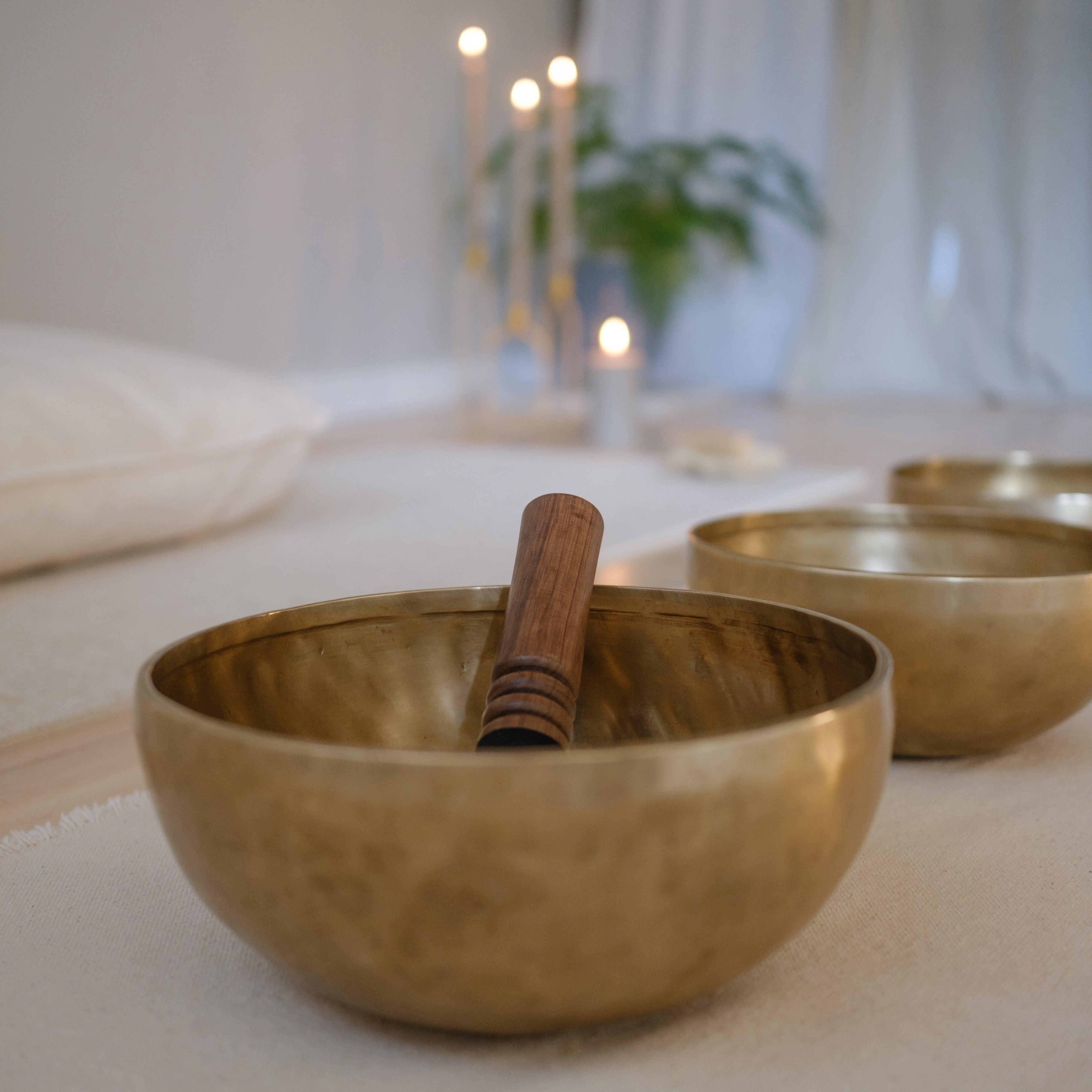 Many dim singing bowls on a white surface with blurred candles and plant in the background