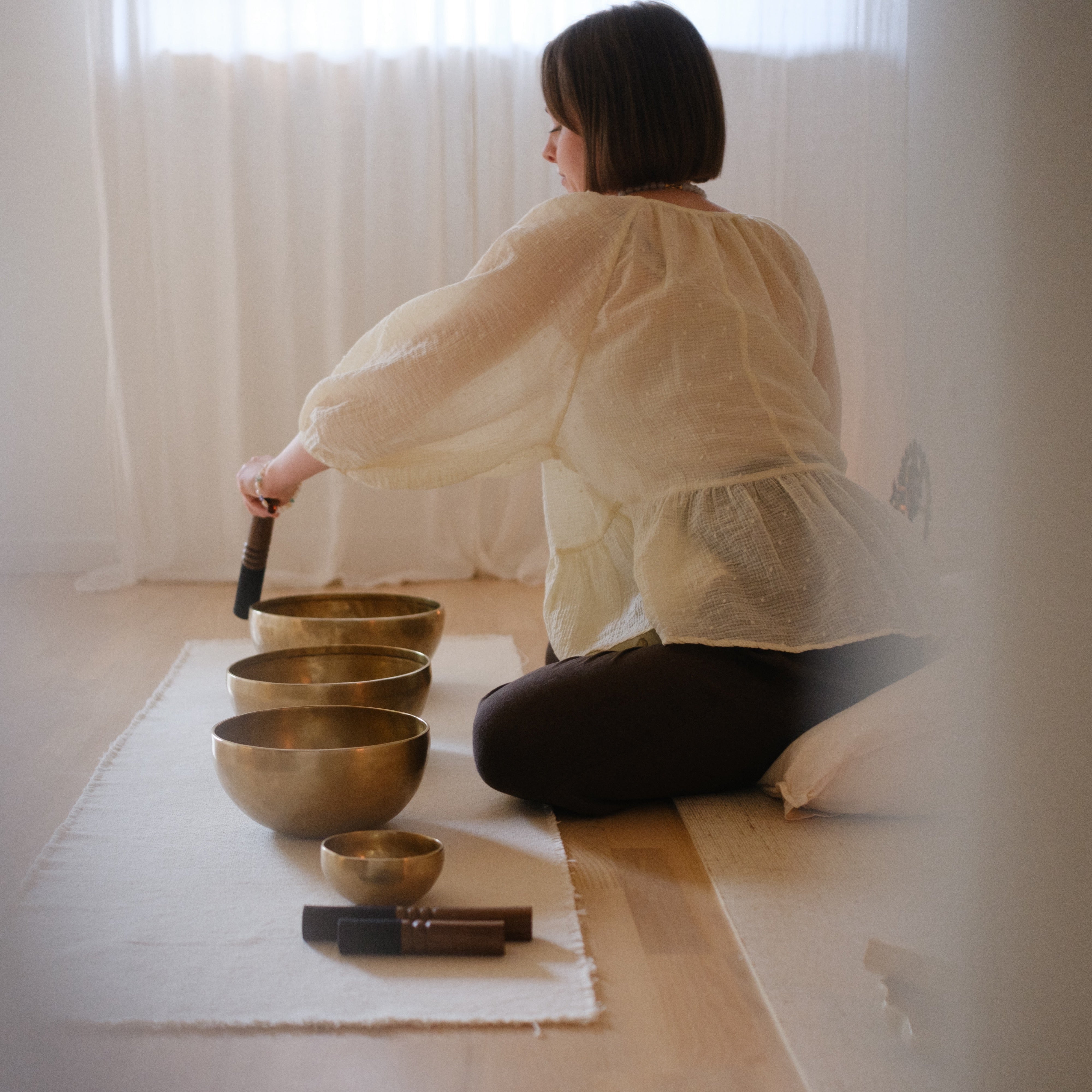 Person sitting on the floor with dim singing bowls in a softly lit room