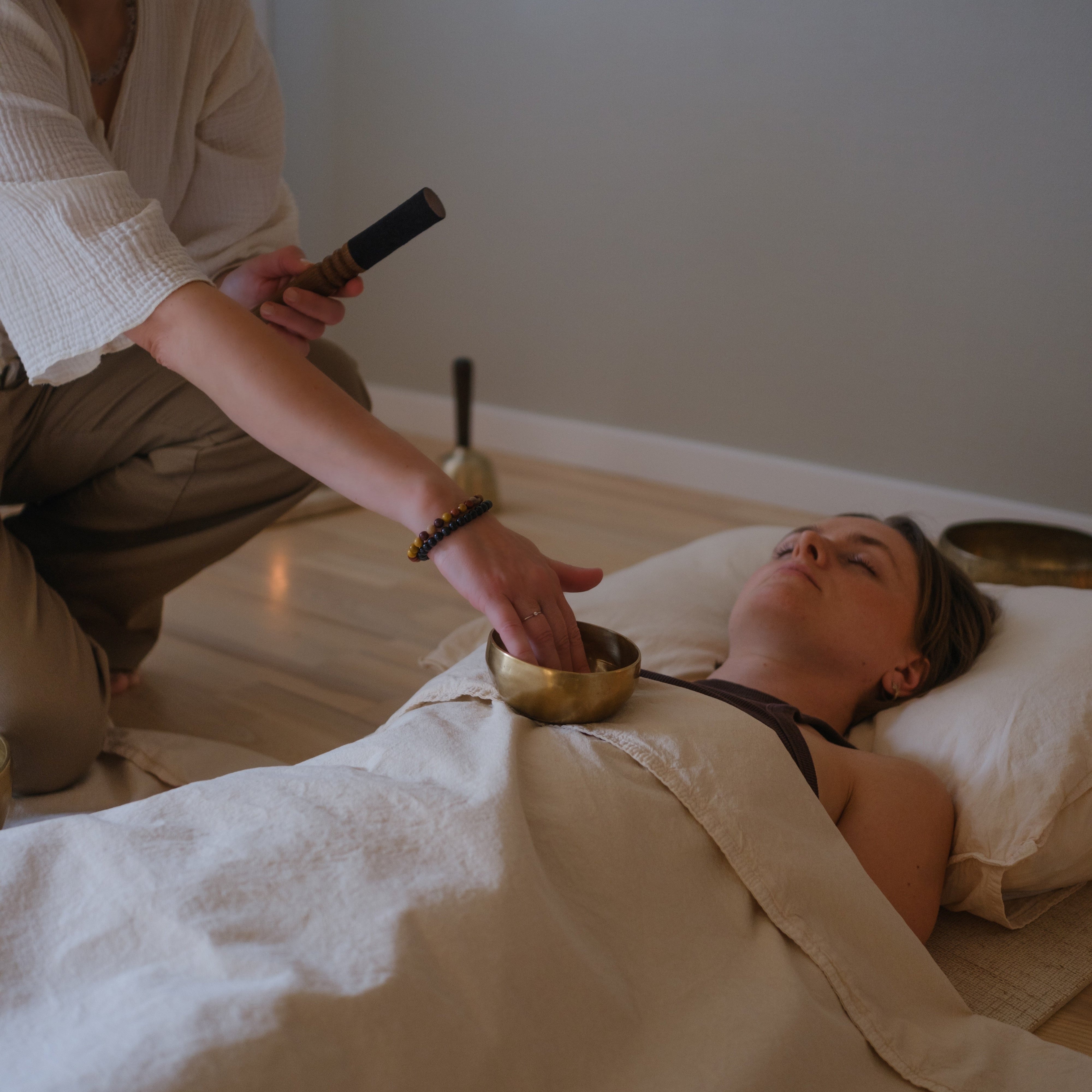 Person receiving sound healing treatment with a small dim singing bowl held by another person in a serene setting.