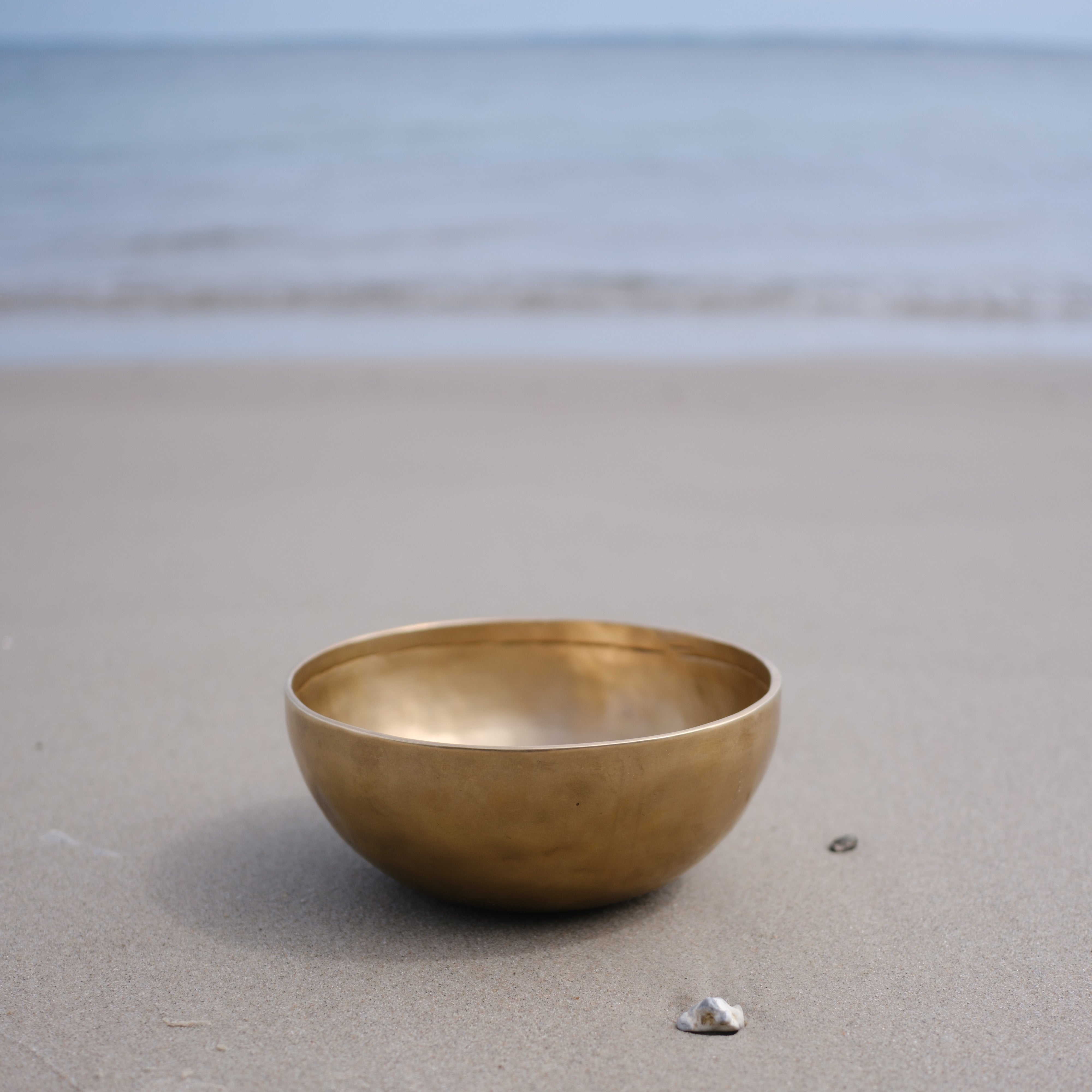 Lingam Singing bowl on a sandy beach with ocean in the background