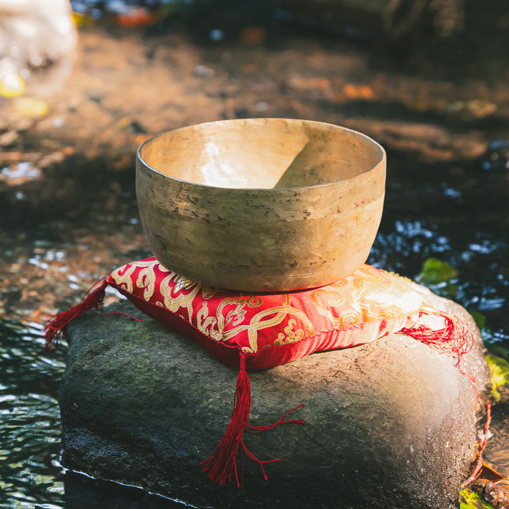 Antique Bronze singing bowl on a rock by a stream