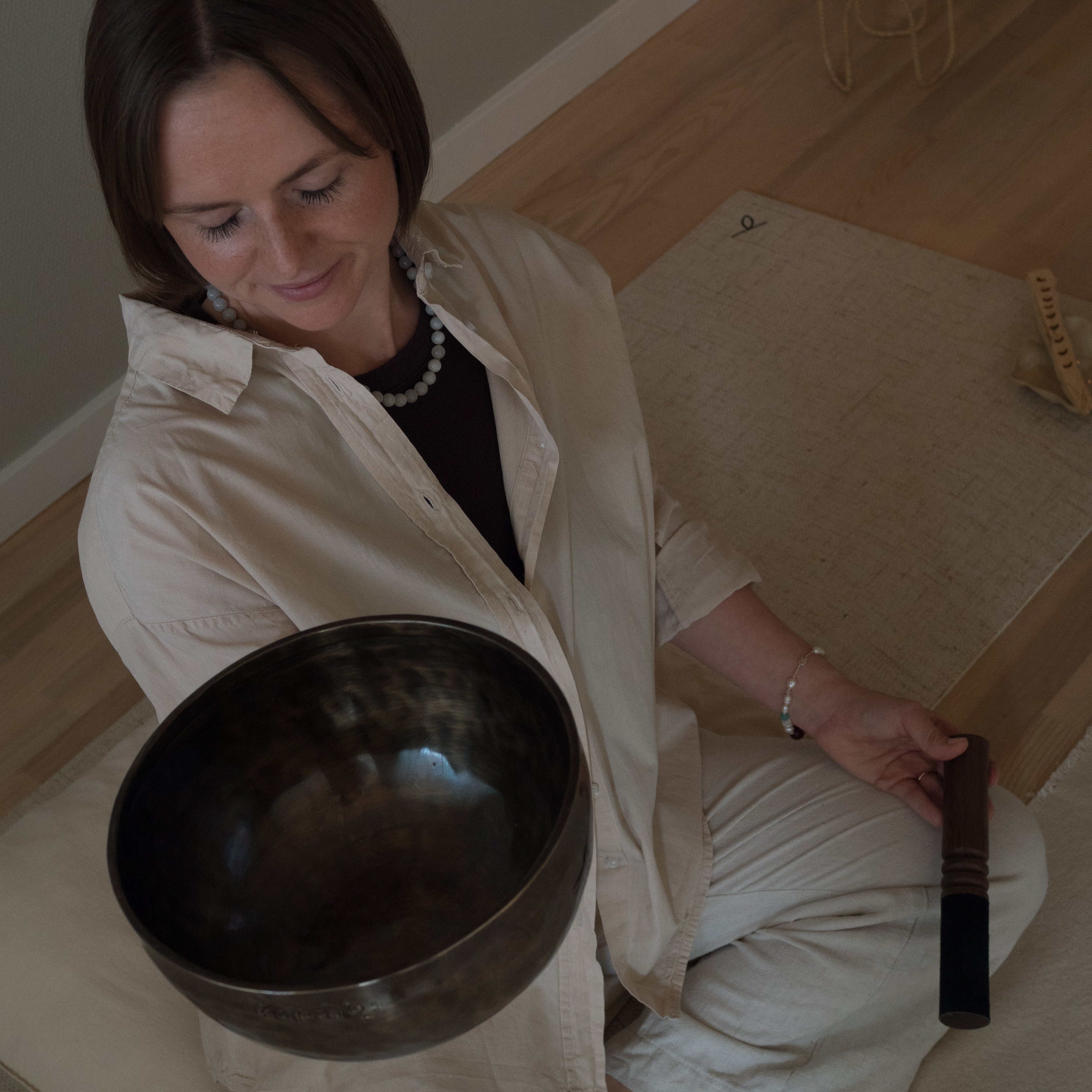 Woman holding a large lunar energy singing bowl in a room with wooden floor and white walls.
