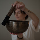 Person holding a lunar energy singing bowl with a wooden mallet against a neutral background