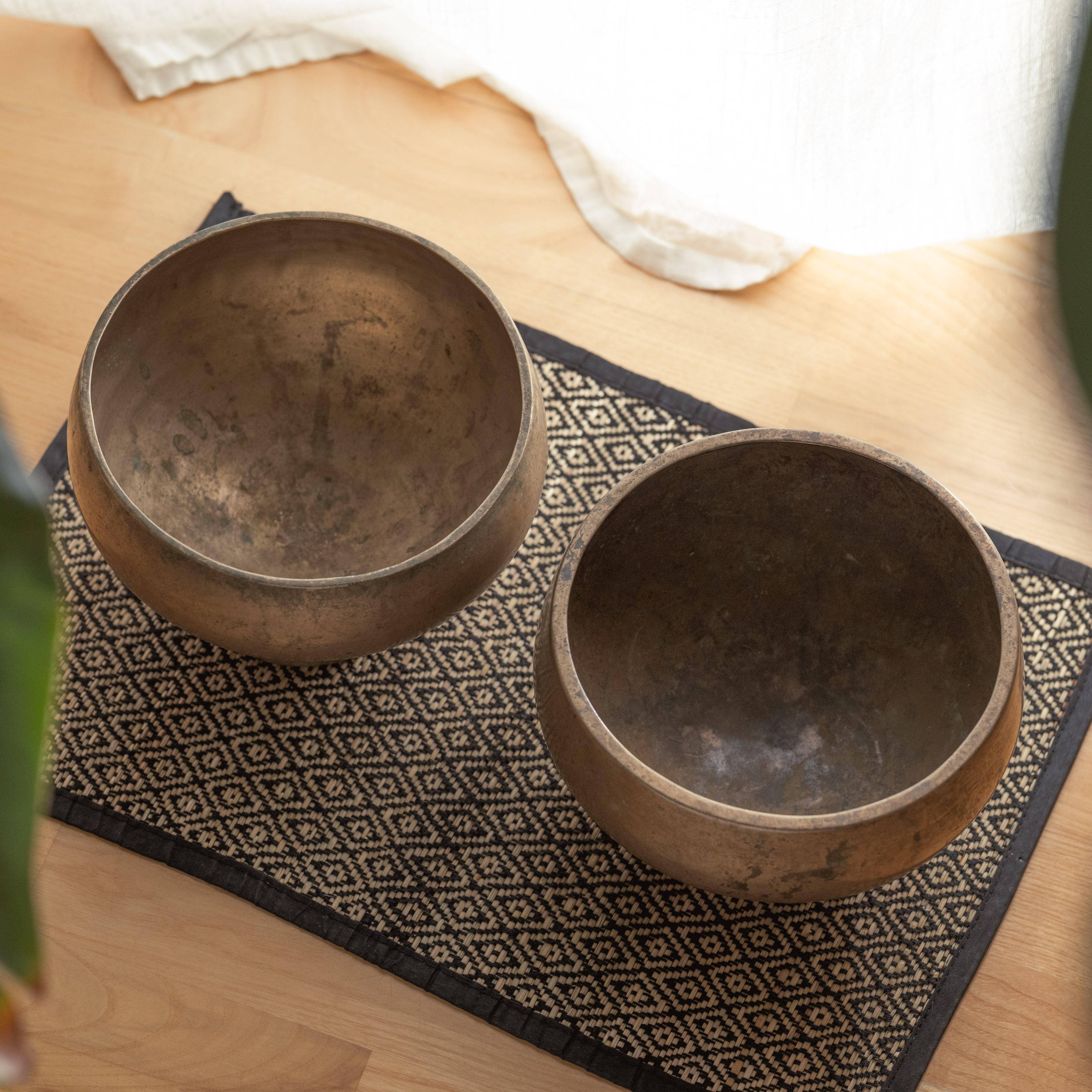 Two antique singing bowls on a patterned mat with a light background