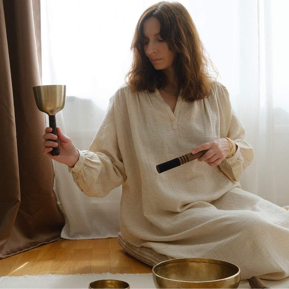 Woman in a white dress holding a singing bowl in a softly lit room.