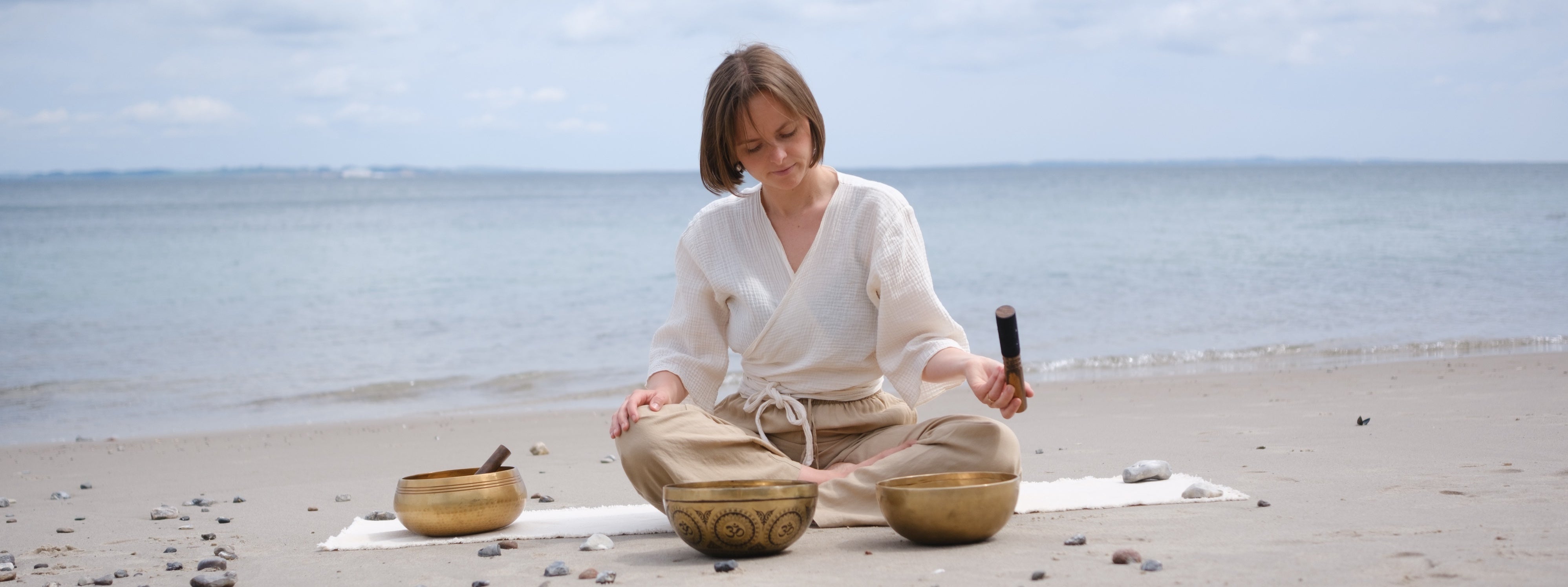A woman playing couple of singing bowls sitting on a beach 