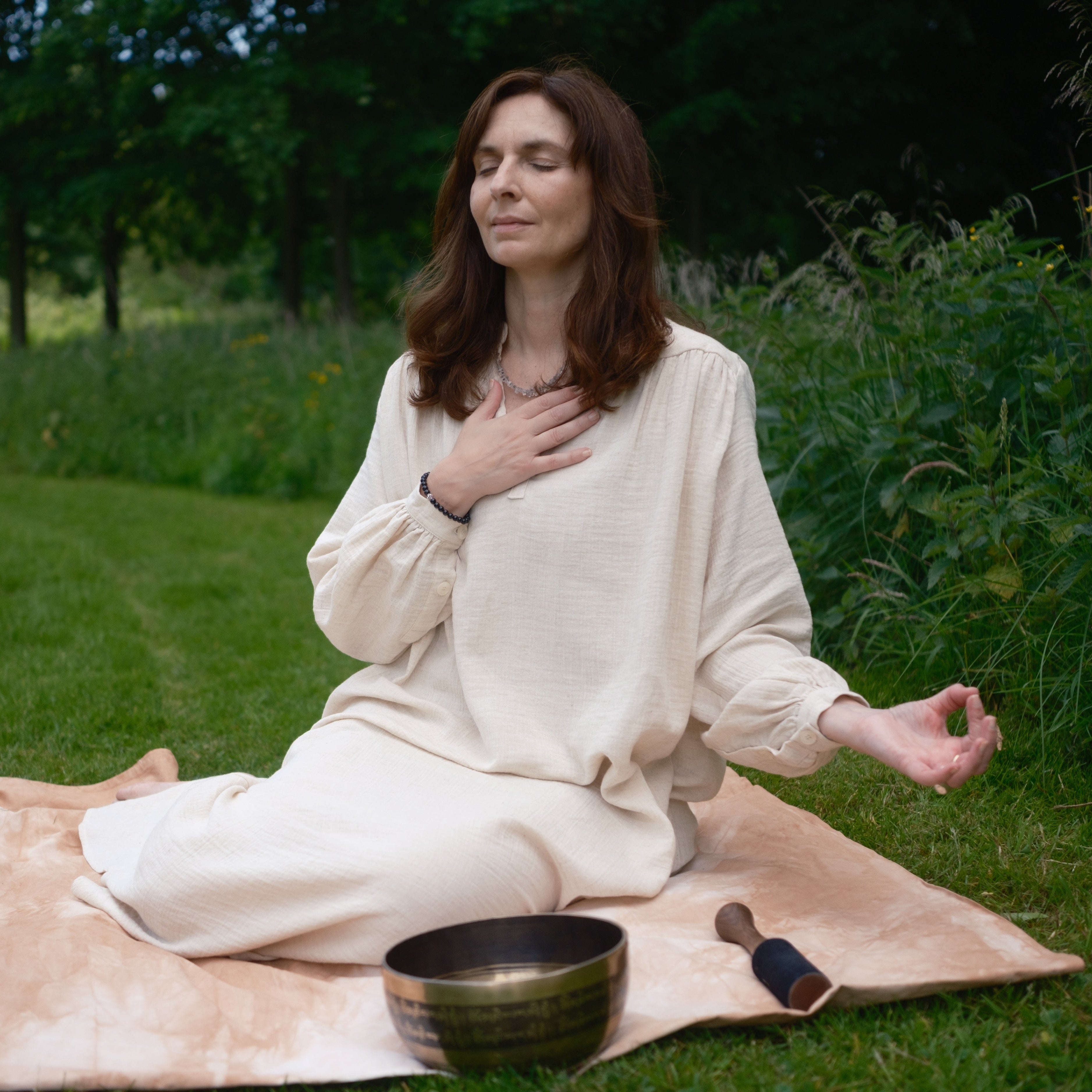 Woman meditating outdoors on a blanket with a singing bowl in front of her.