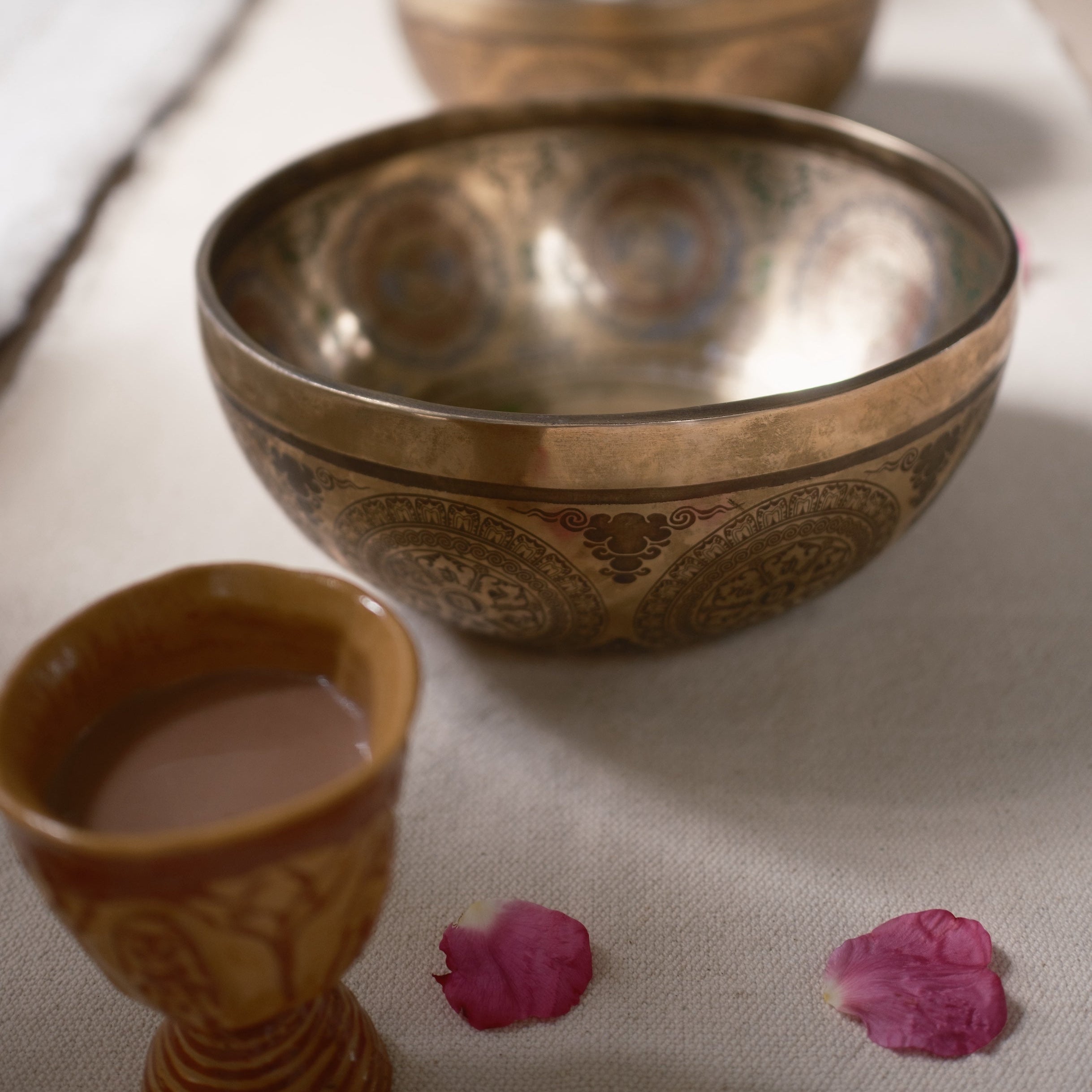 Decorative singing bowls and a cup on a textured surface with pink petals.