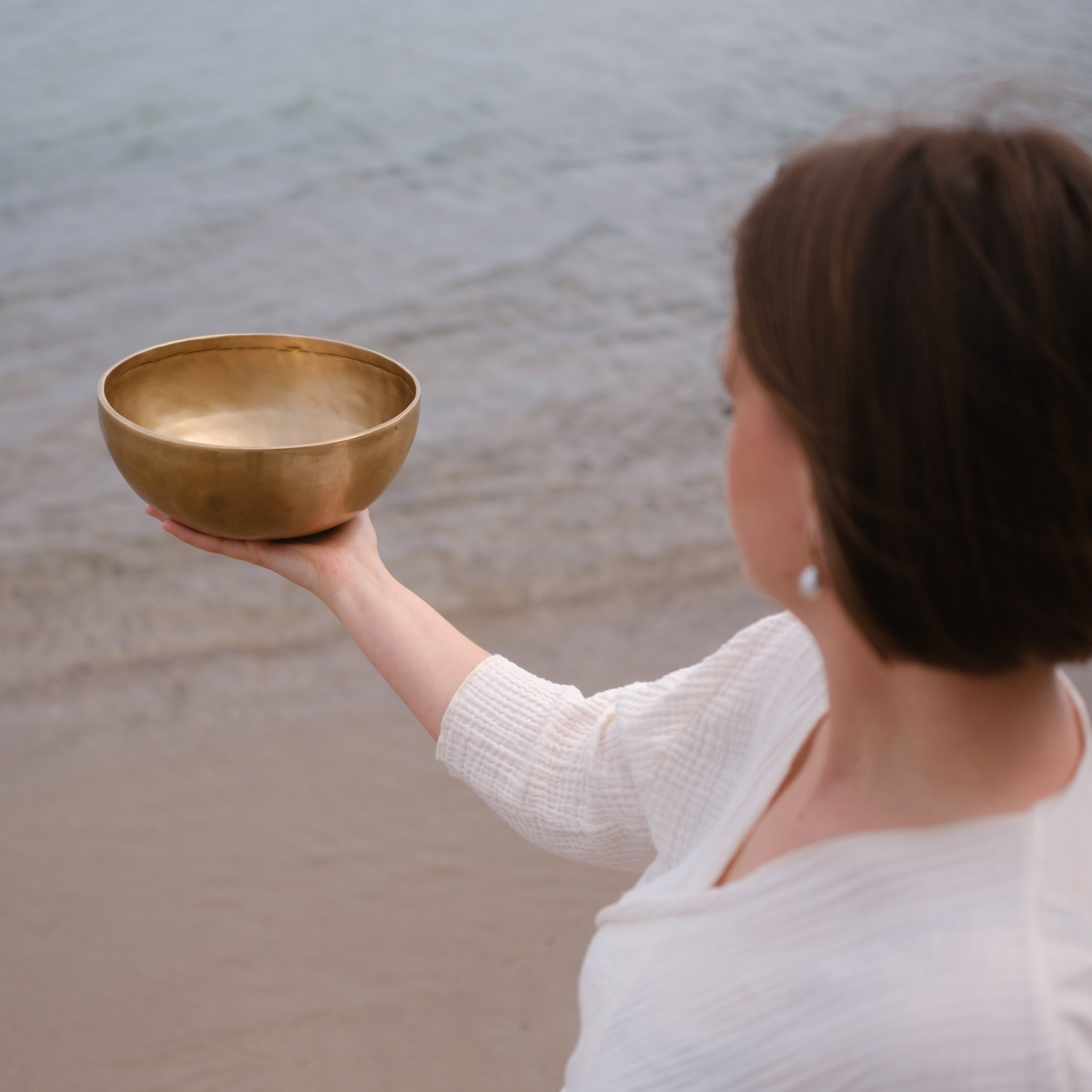 Person holding a lingam singing bowl on a beach