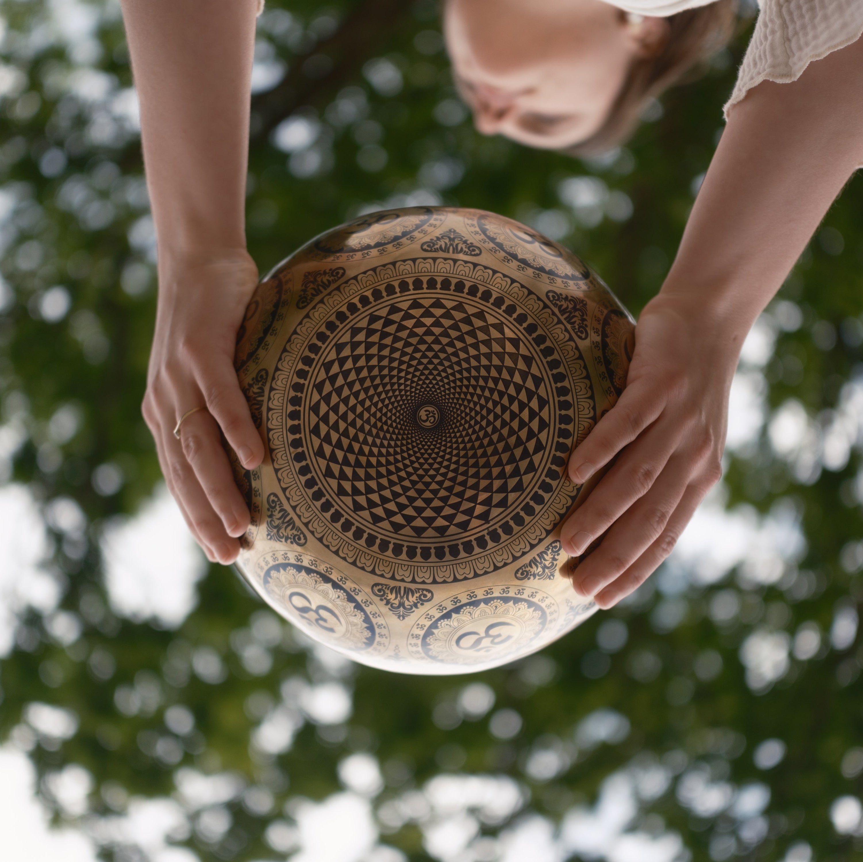 Person holding a tara buddha singing bowl with blurred green foliage in the background
