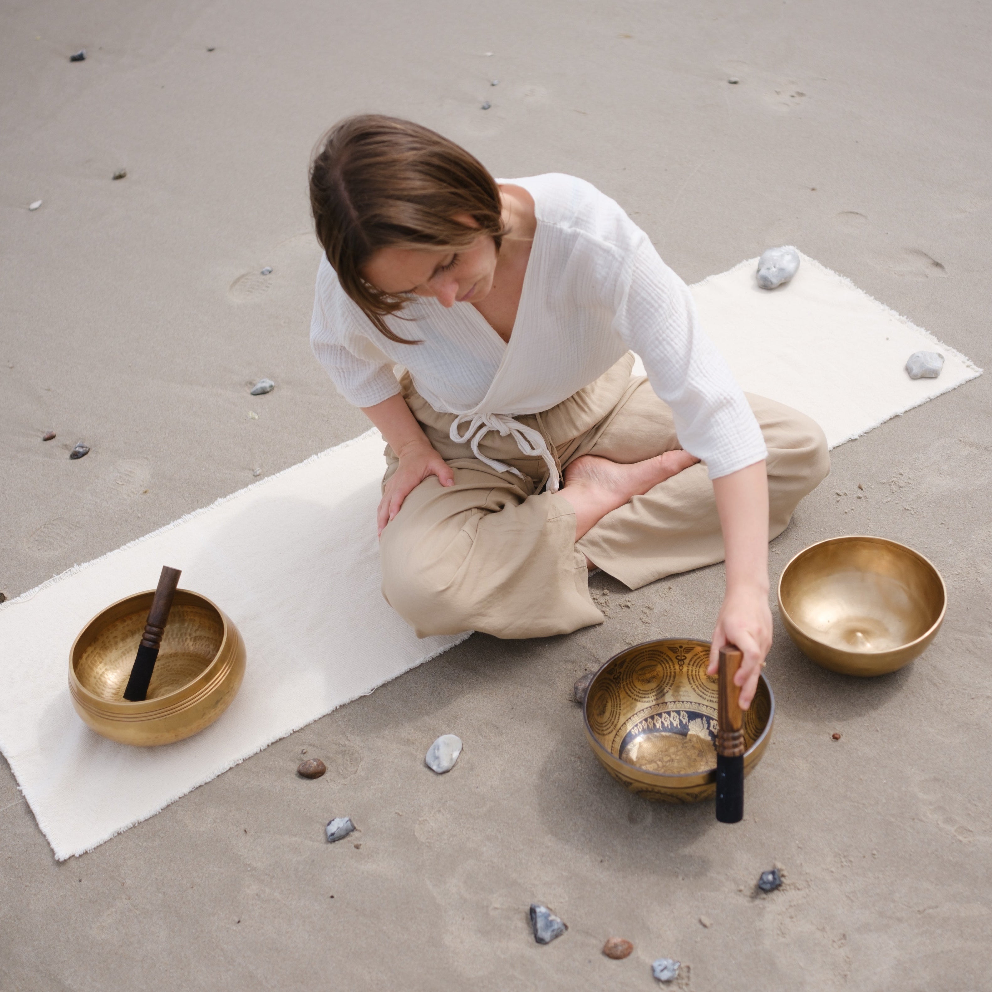 Person playing singing bowls on a mat outdoors