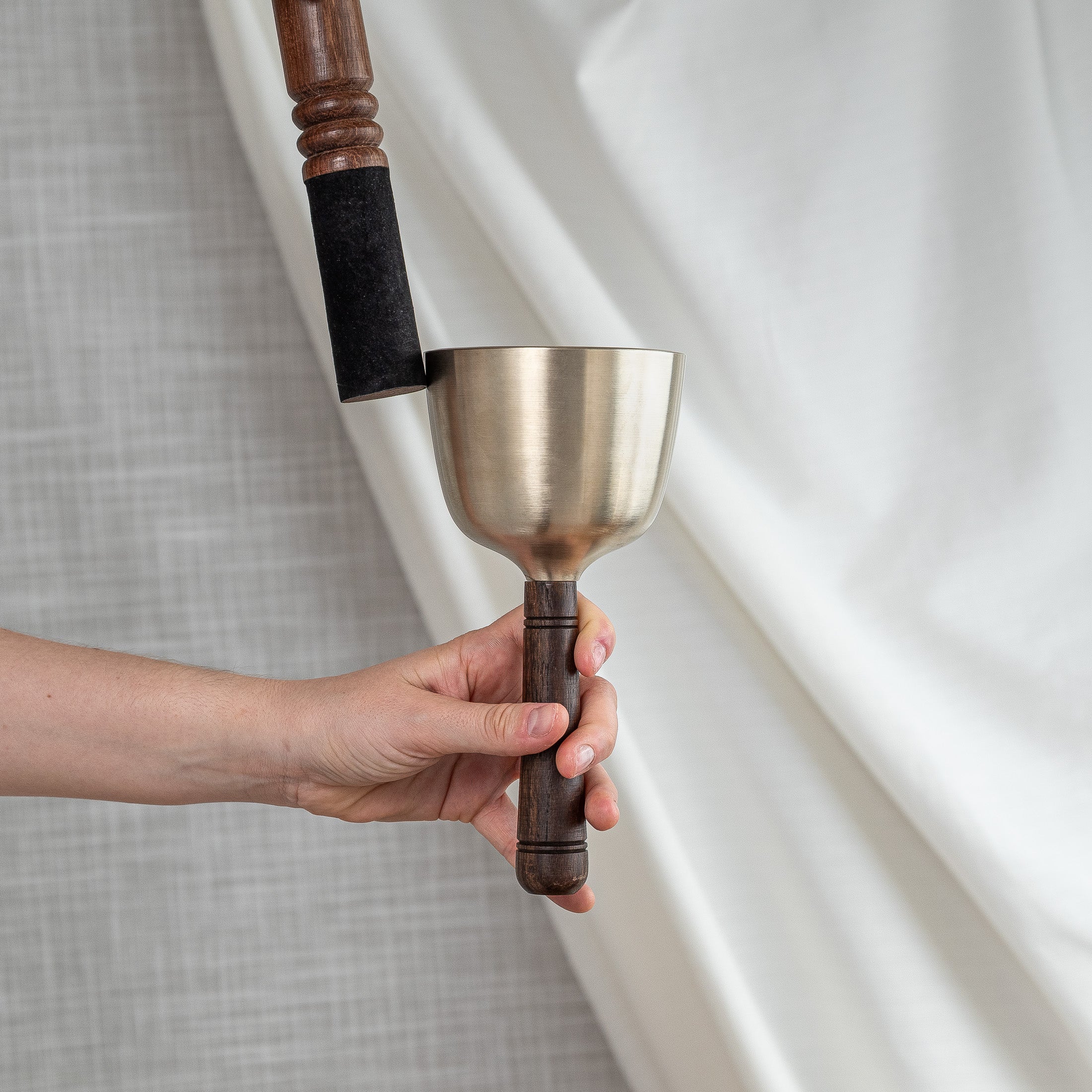 Person holding singing bowl with wooden handle facing downwards