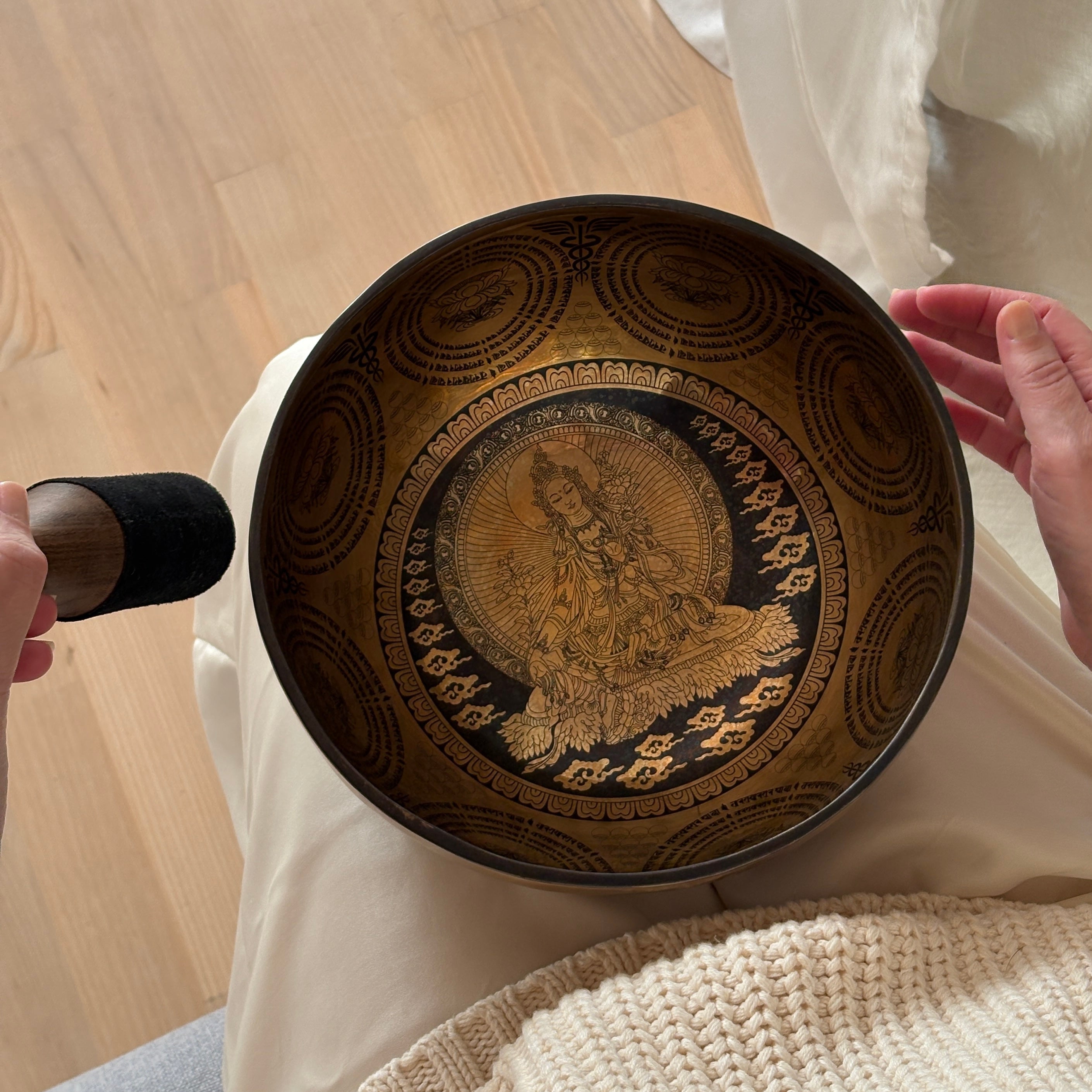 Etched singing bowl with intricate design held by a person on a wooden surface