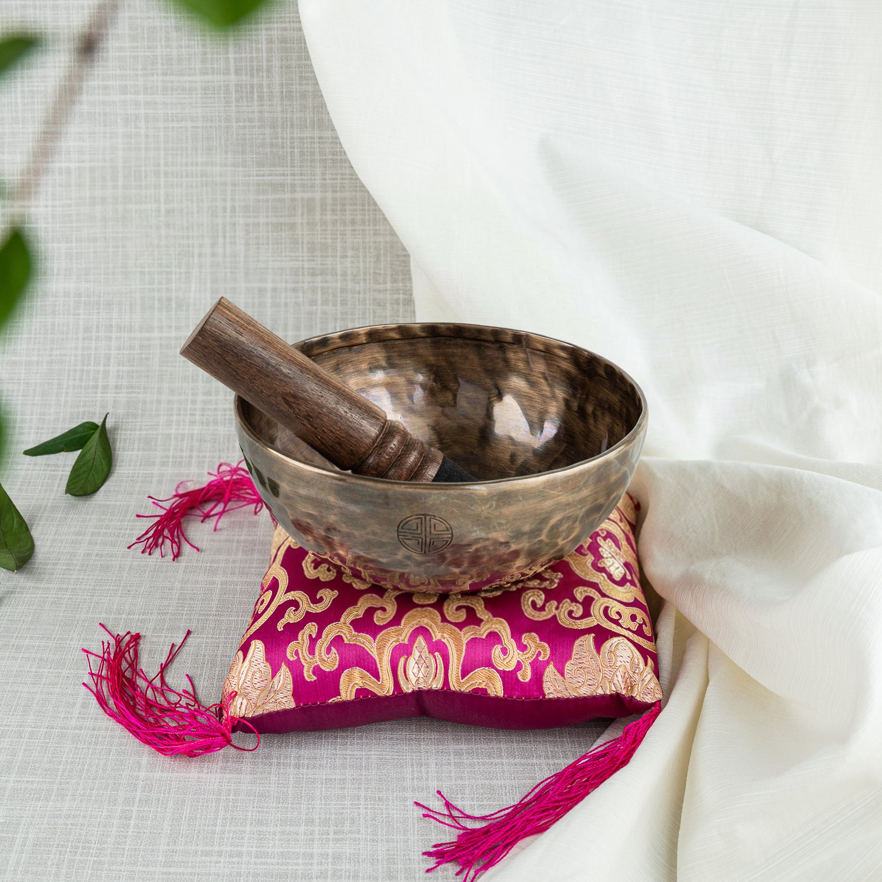 Tibetan singing bowl with wooden striker on a decorative pillow with tassels