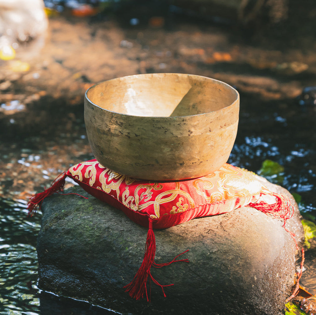 Antique Bronze singing bowl on a rock by a stream